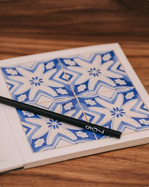 Blue and white tile design with black pencil on wooden table.