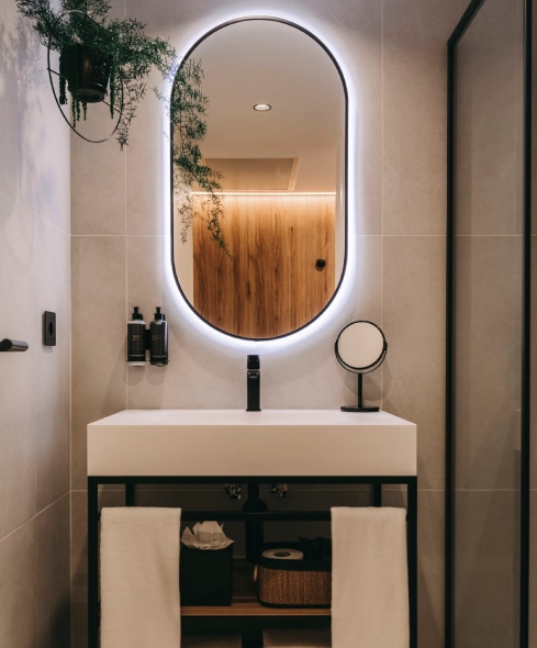 Modern bathroom with an oval backlit mirror and a sleek white sink with black accents.