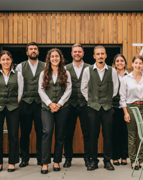 Seven people in matching vests smiling in front of a wooden wall.