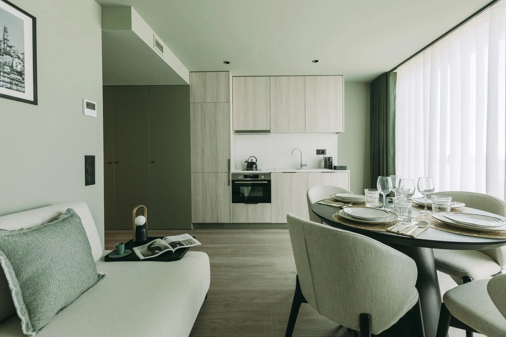 Modern kitchen with dining table, sofa, and large window with sheer curtains.