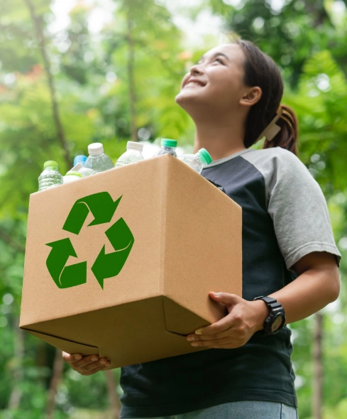 Person holding recycling box filled with plastic bottles outdoors.