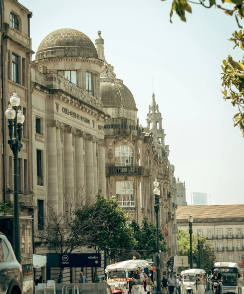 Street scene with historic buildings and a dome, trees, and pedestrians in a European city.