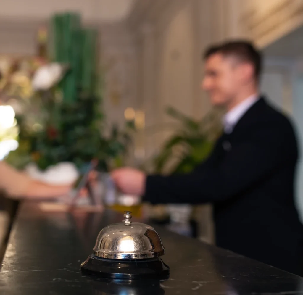 Hotel reception desk with a service bell, a person blurred in the background.