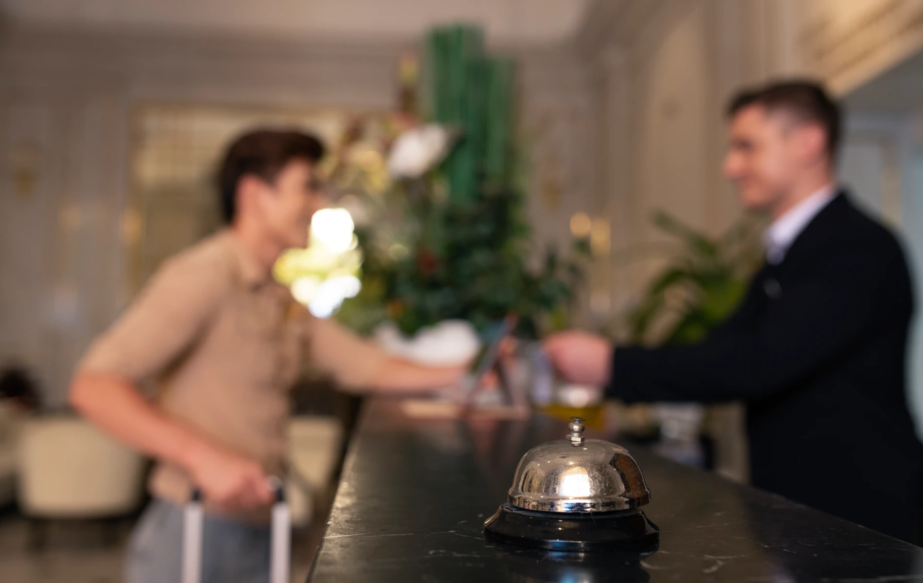 Hotel reception with focus on service bell, two men interacting in the background.
