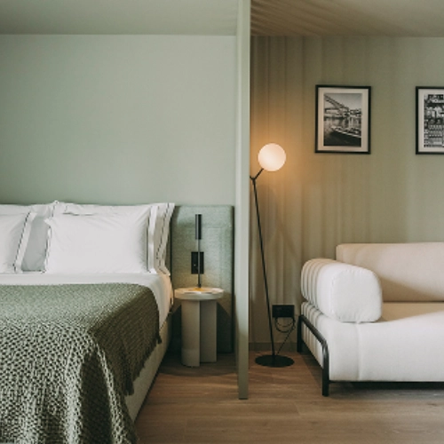 Minimalist bedroom with a bed, a lamp, a white sofa, and framed photos on the wall.