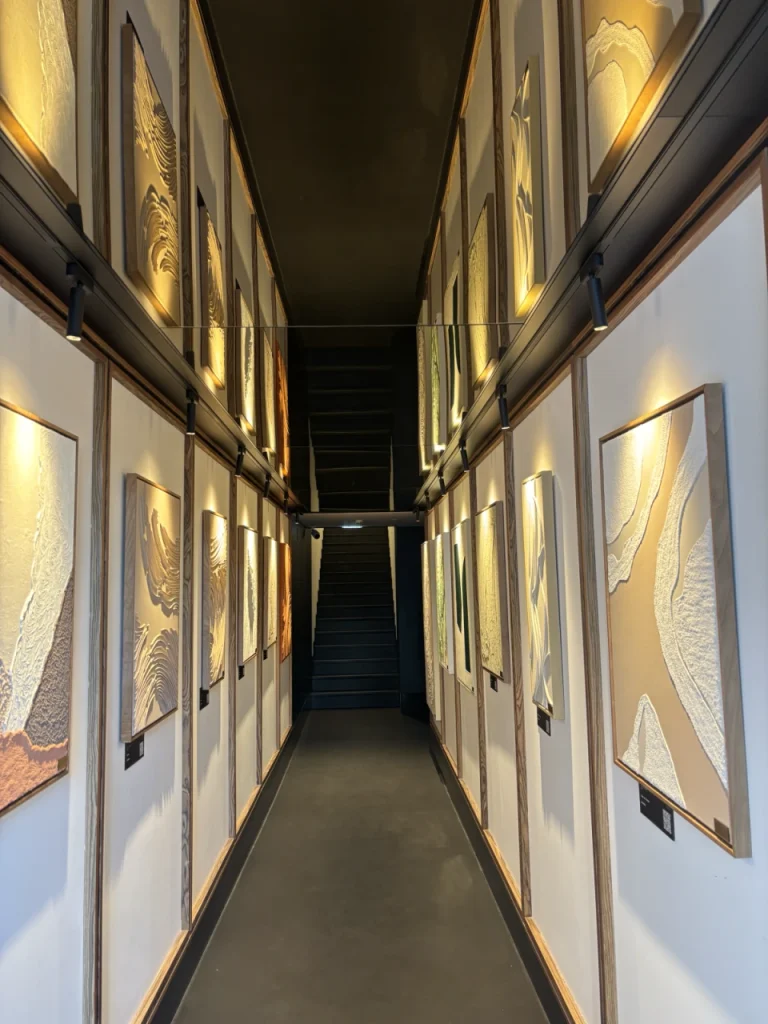 A narrow hallway with framed abstract artworks on both walls, leading to a staircase.