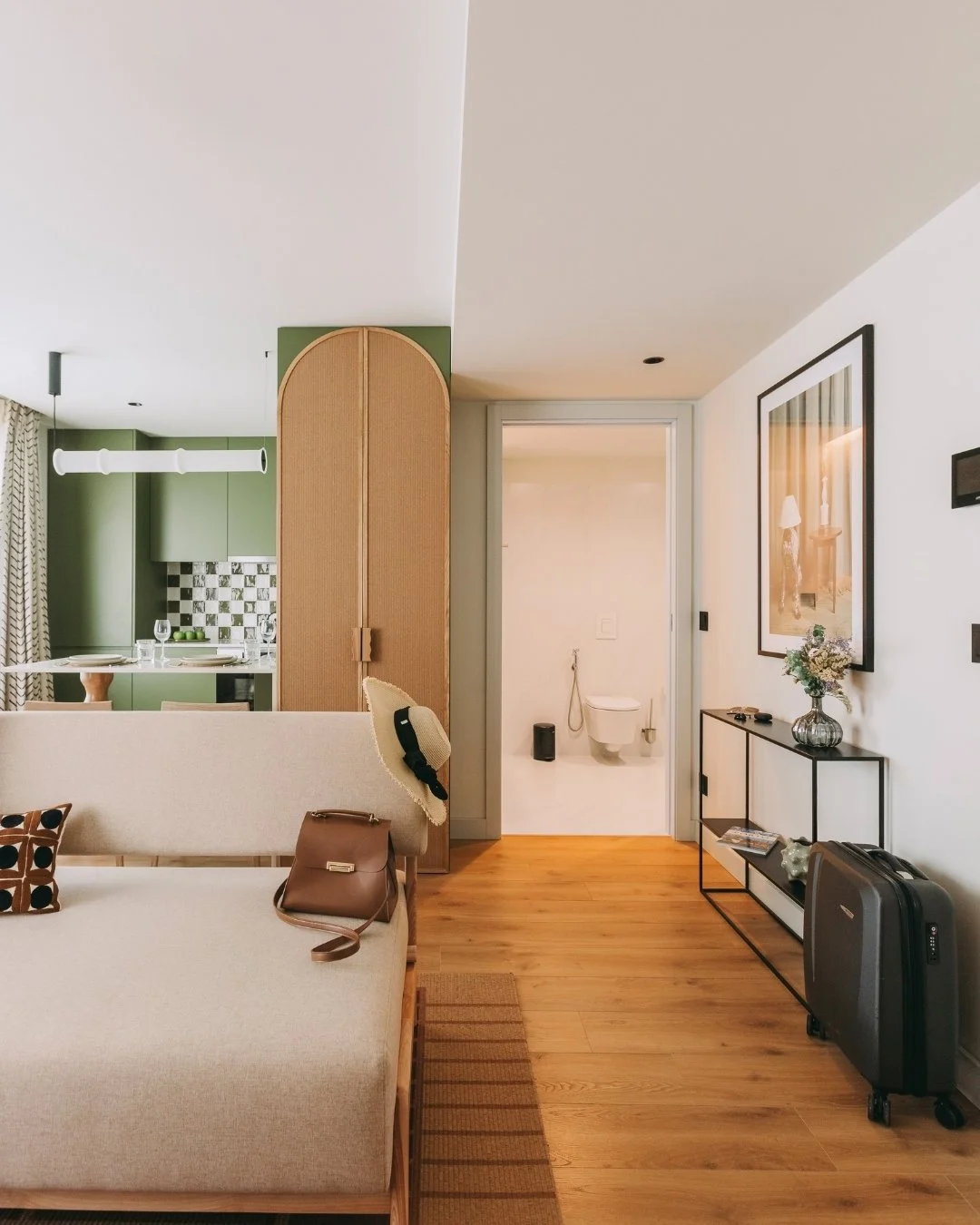 Modern apartment interior with sofa, kitchen, and hallway to a bathroom. Suitcase by the door.