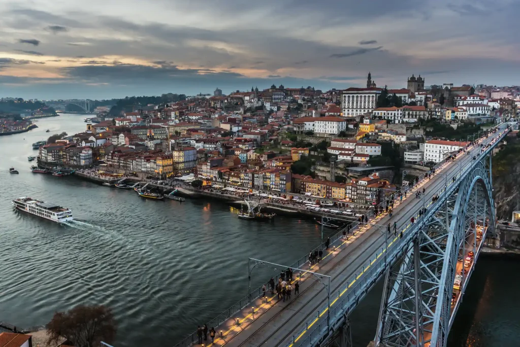 A scenic view of Porto, Portugal with a bridge and riverside buildings at sunset.