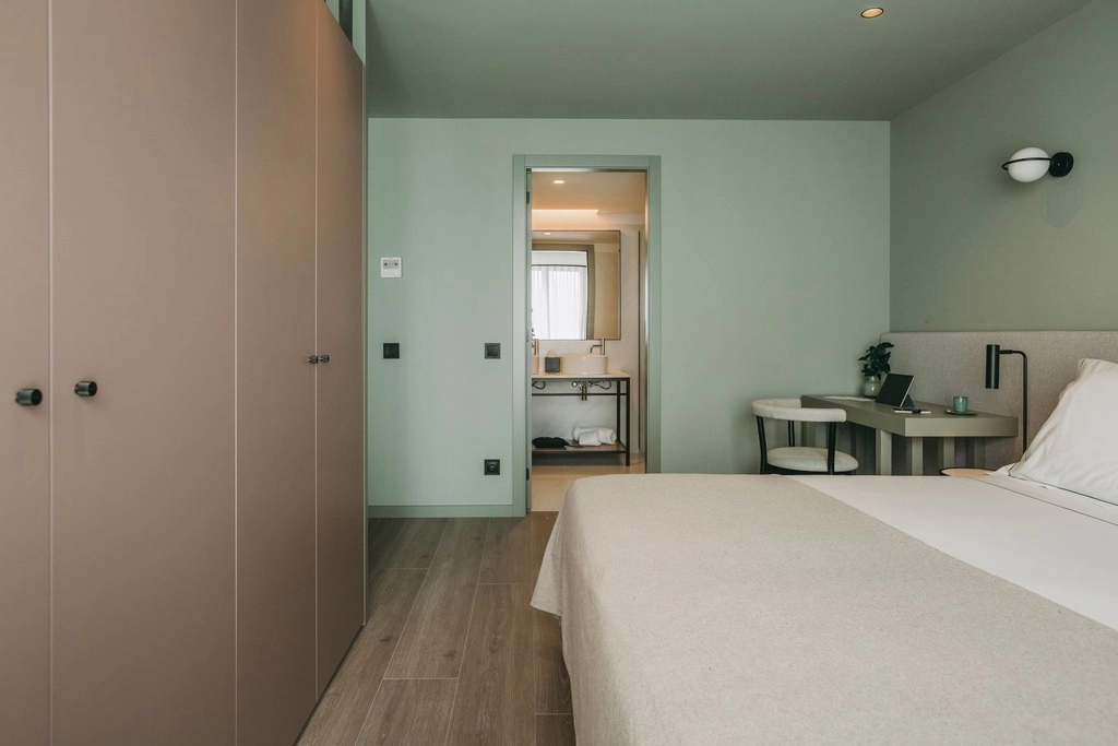 Minimalist hotel room with a bed, desk, and bathroom in the background.