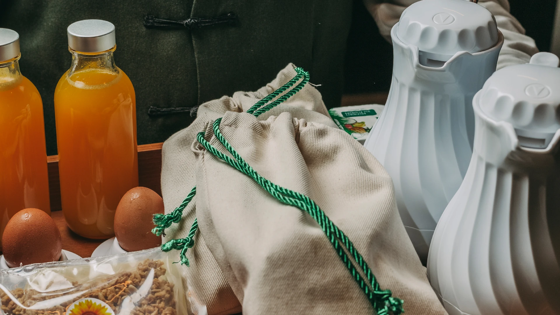 Bottled juice, eggs, cloth bags, and white containers on a table.