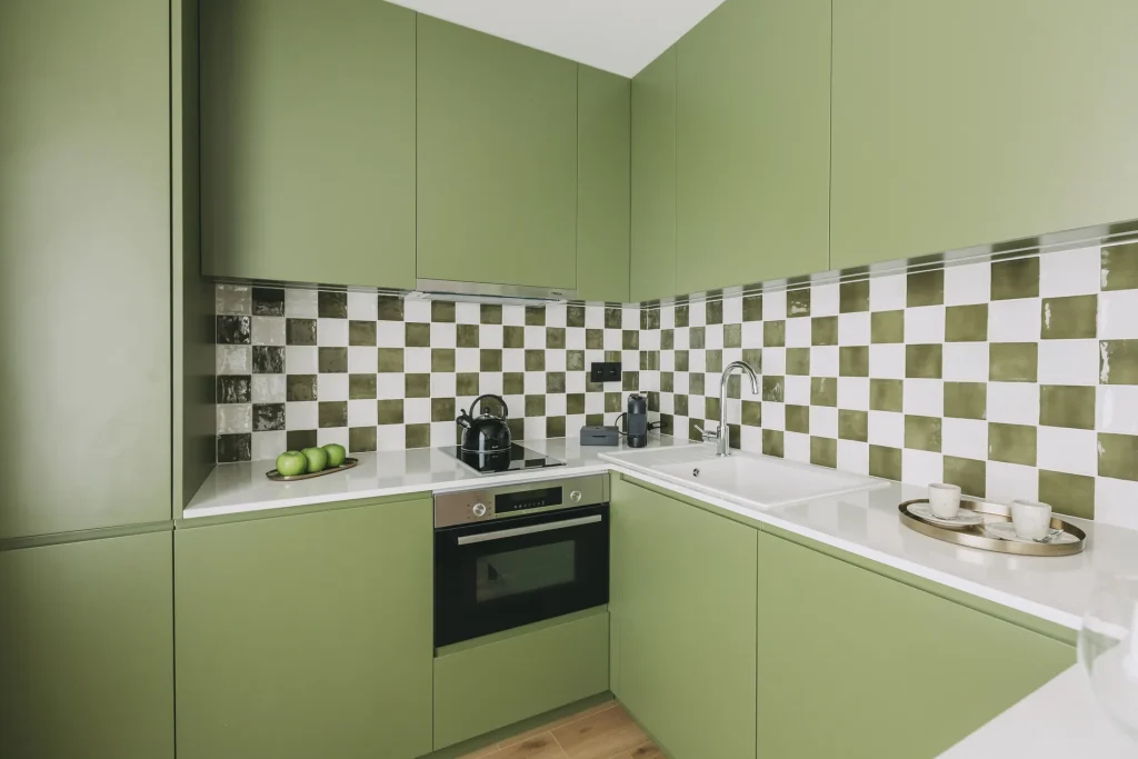 Green kitchen with checkered backsplash, modern appliances, and neatly arranged items.