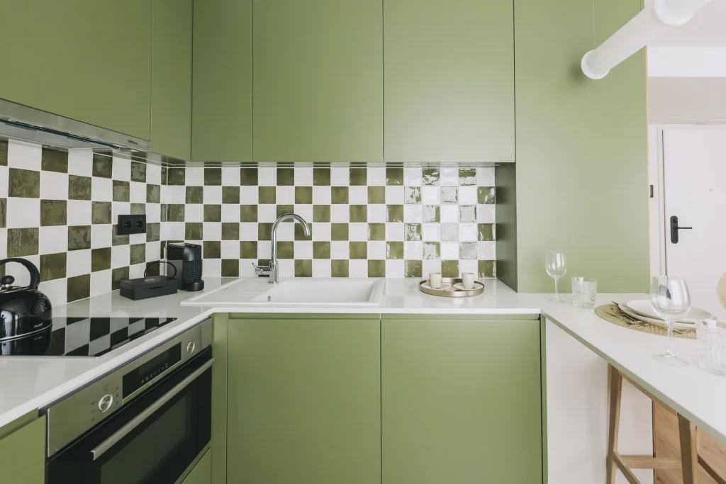 Modern kitchen with green cabinets and checkered backsplash.