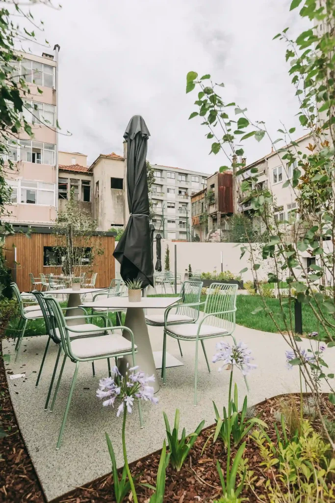 Outdoor patio with green furniture, plants, and a closed umbrella in a garden setting.