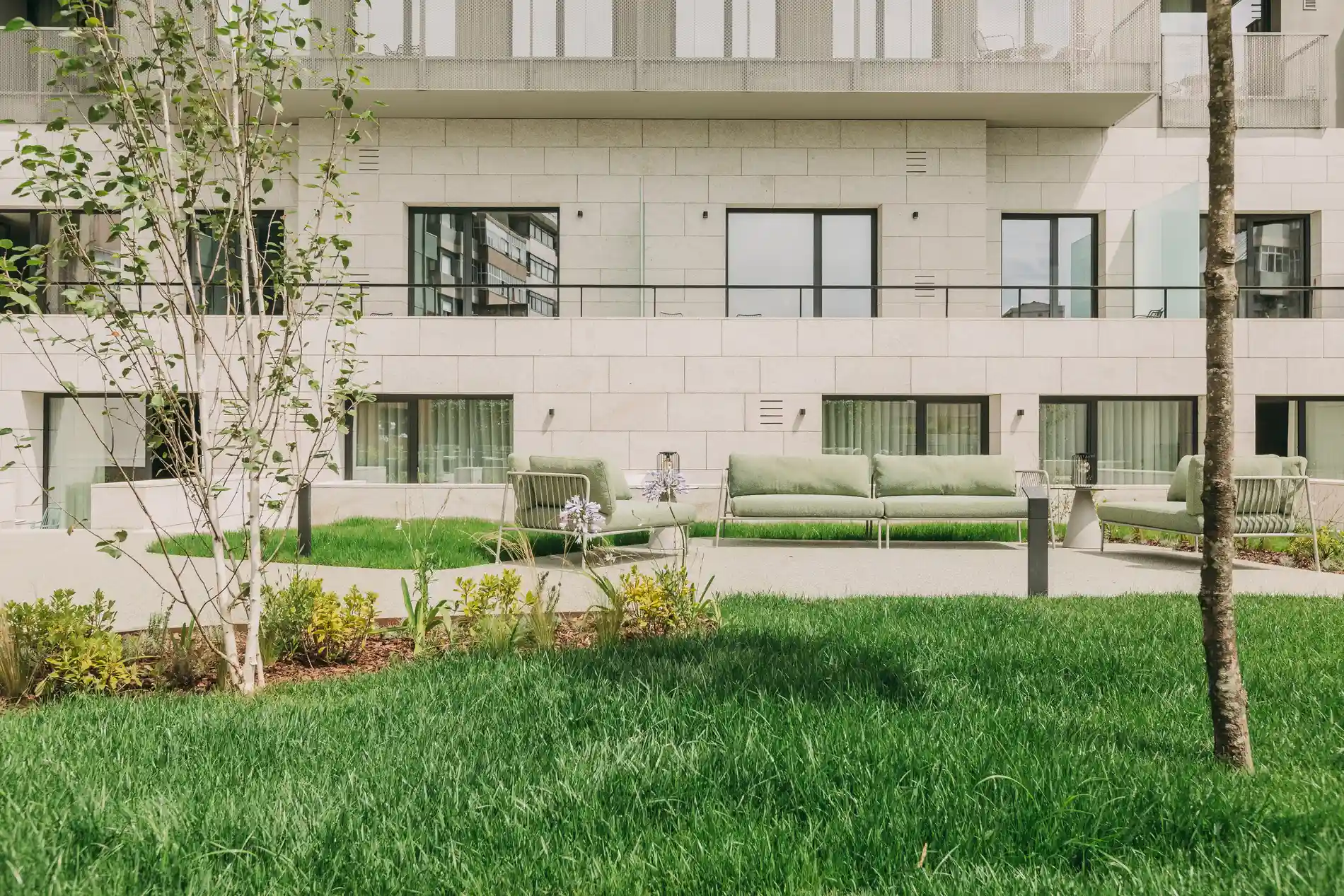 Green lawn with trees and outdoor seating in front of a modern apartment building.