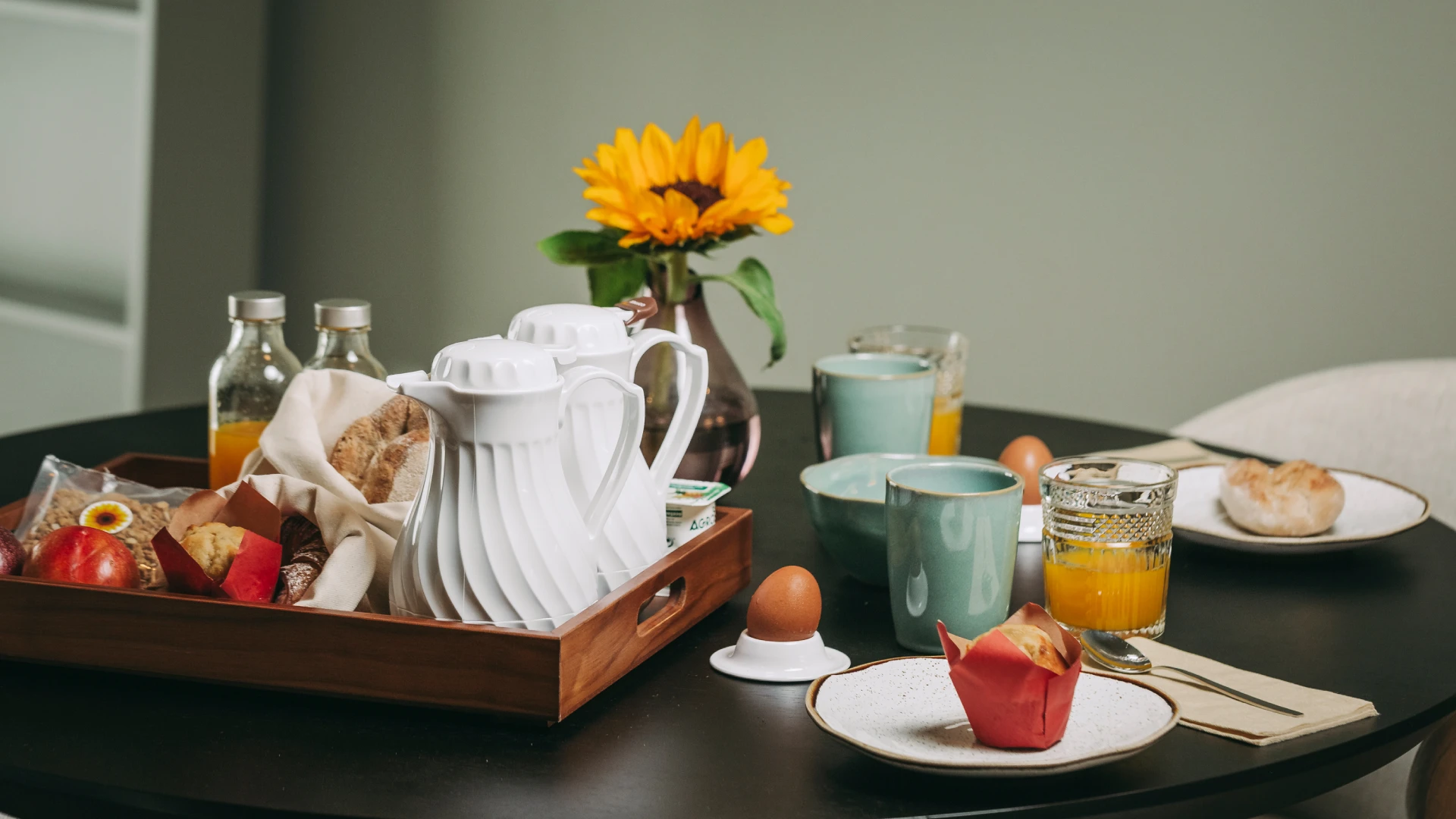 Breakfast table with pastries, coffee, juice, and a sunflower in a vase.