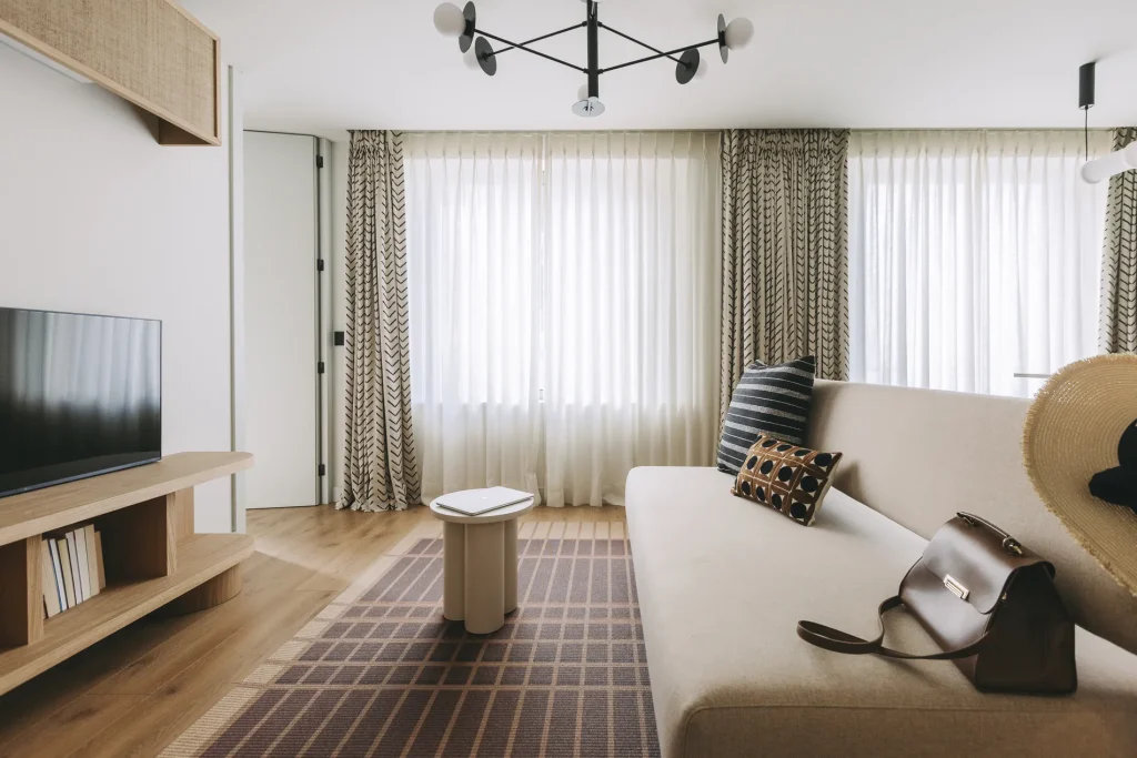 Minimalist living room with a beige sofa, TV, rug, pillows, and a bag on a table.