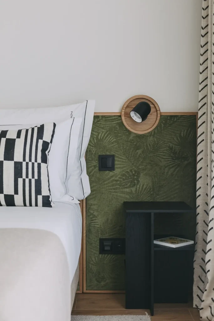 Bedside with green wall, black lamp, patterned pillow, and a nightstand with a book.