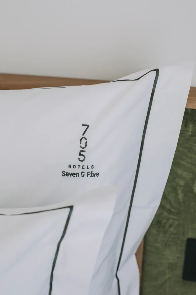 White pillowcase with "705 Hotels Seven O Five" embroidery and black trim.