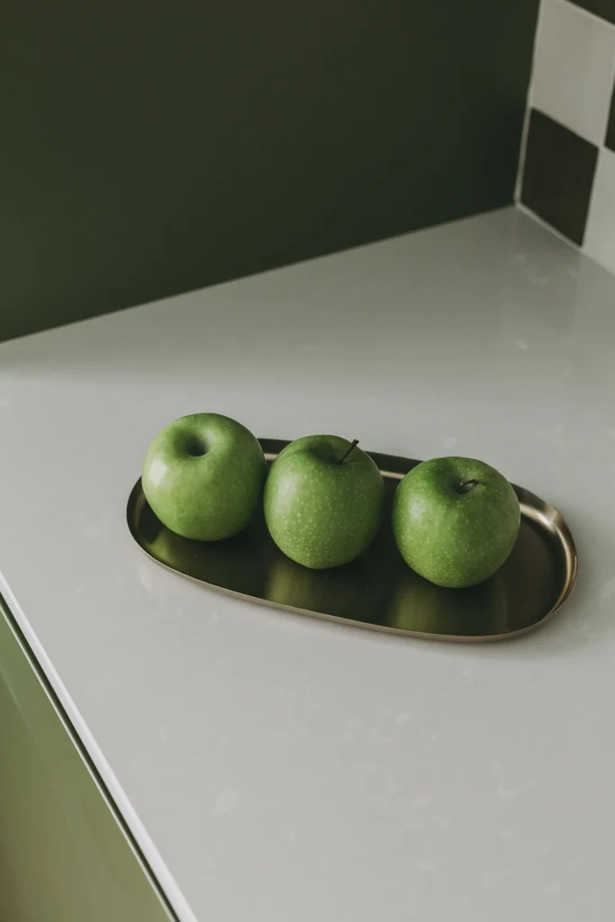 Three green apples on a brass tray on a white countertop.