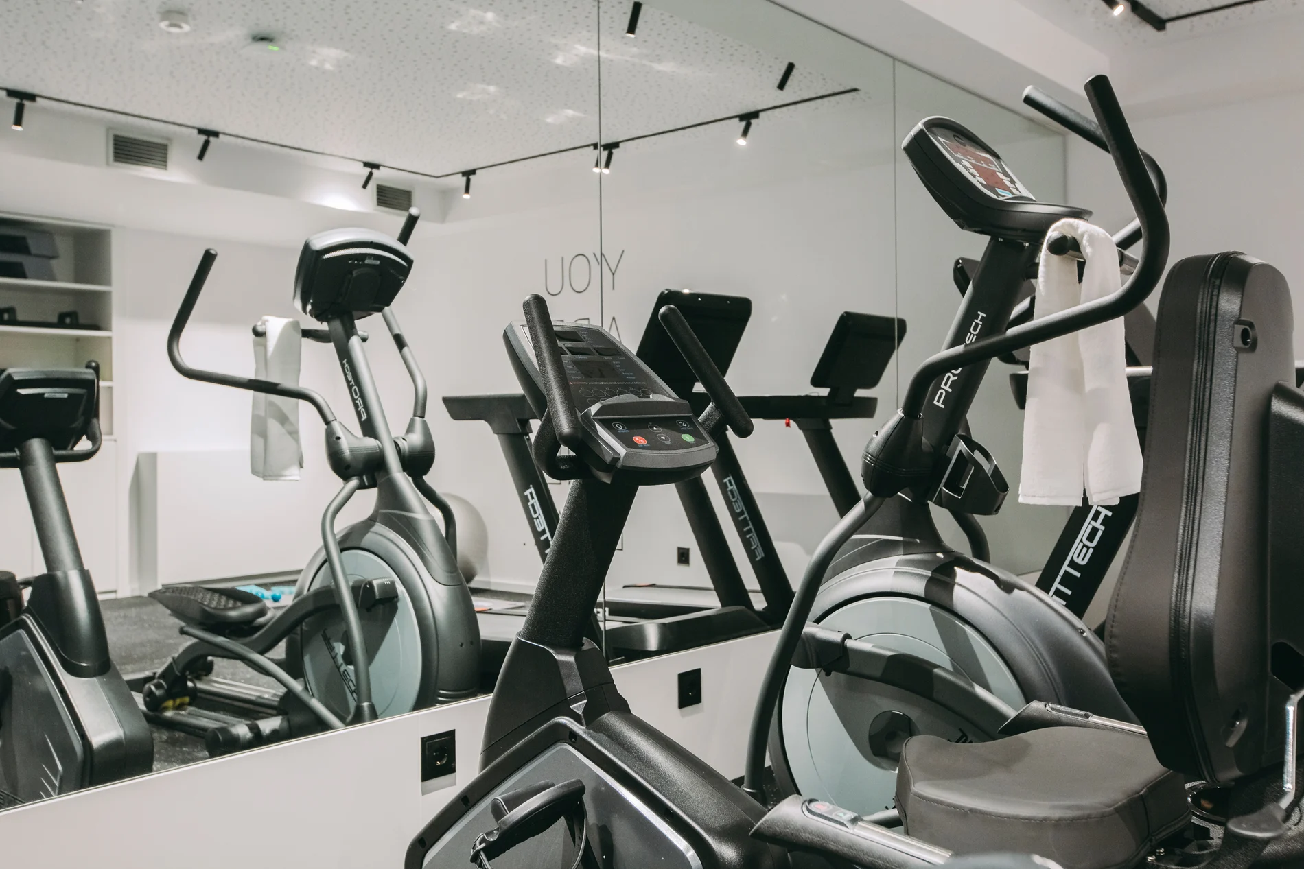 Elliptical machines in a gym with towels hanging on handlebars.