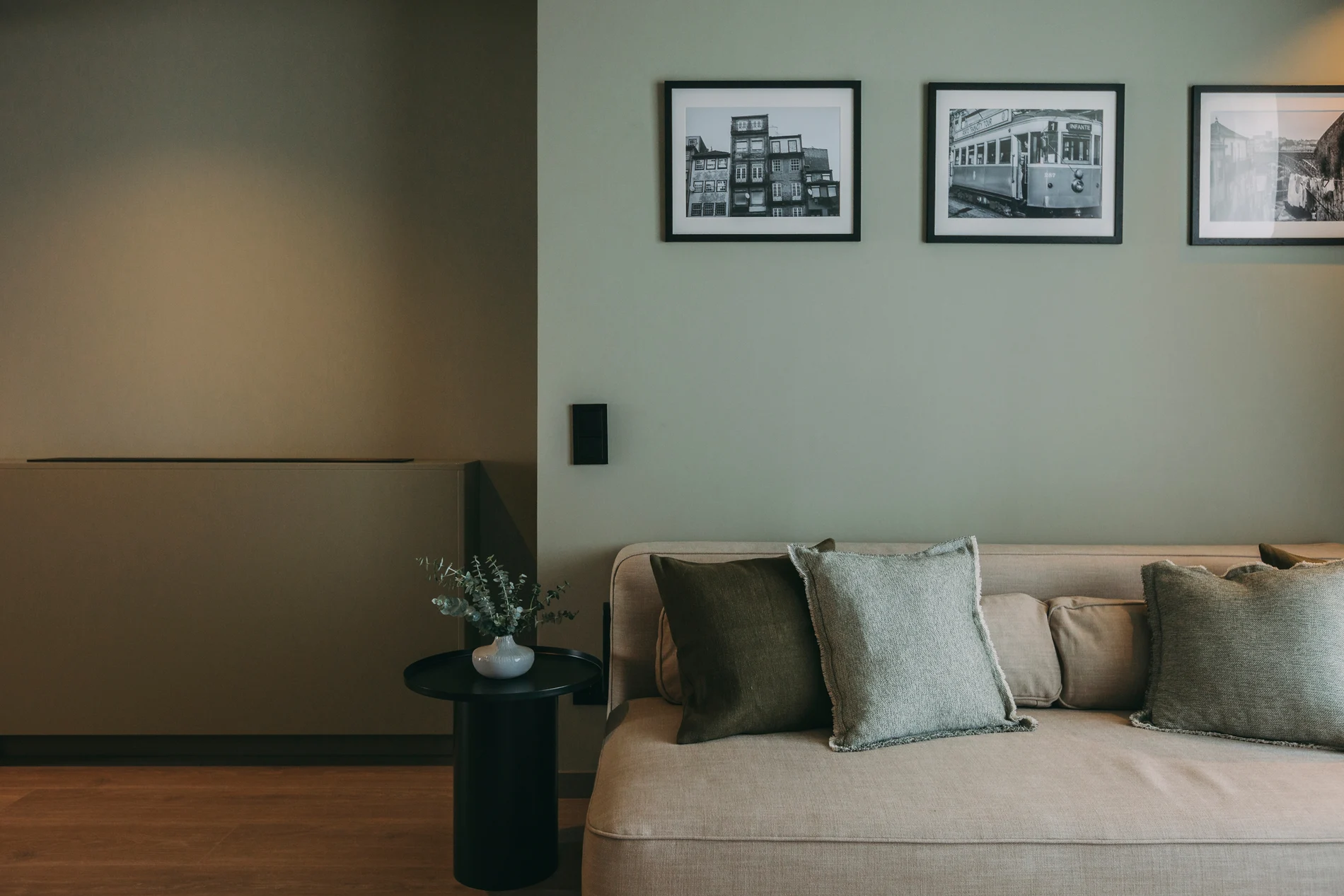 Minimalist room with a beige sofa, cushions, plant, and three black-and-white photos on the wall.