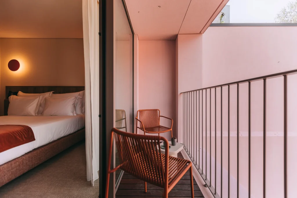 Modern balcony with orange chairs and a table, connected to a cozy room with a bed.