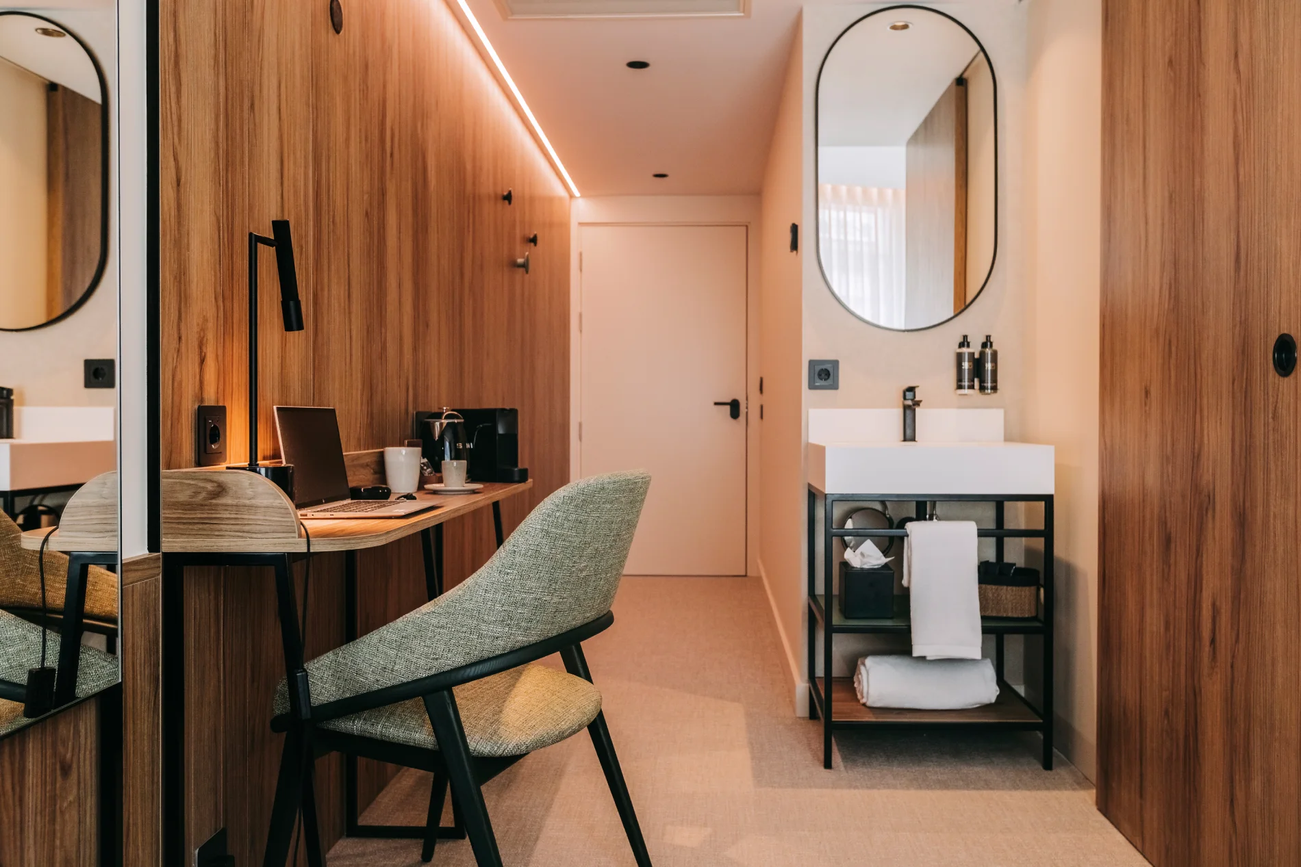 Hotel room with wooden walls, desk, chair, and a small sink with a mirror.