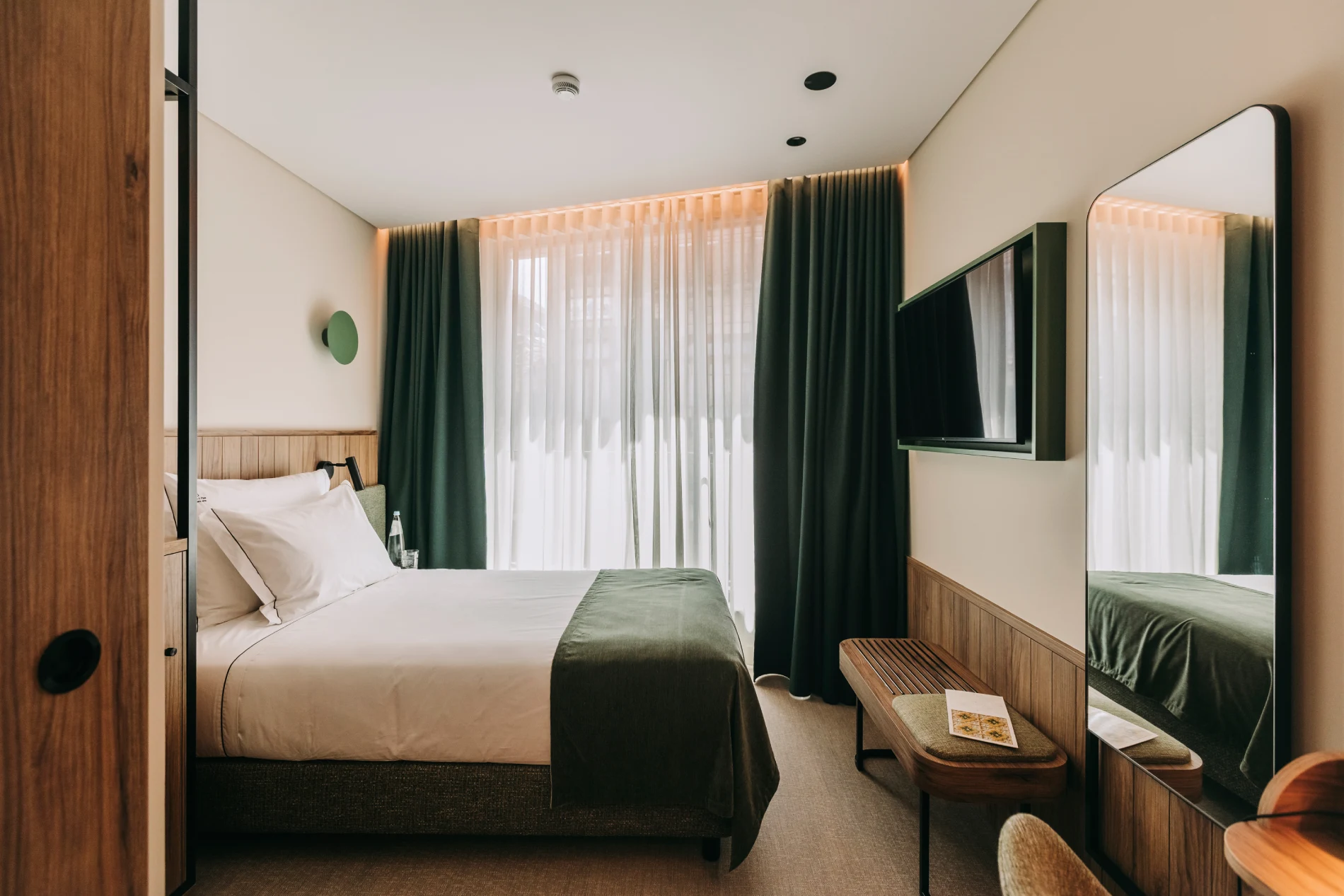 Cozy modern hotel room with a double bed, TV, and large window with dark green curtains.