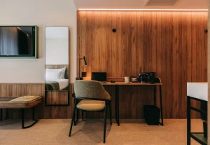 Modern hotel room with desk, chair, TV, mirror, and wooden wall.