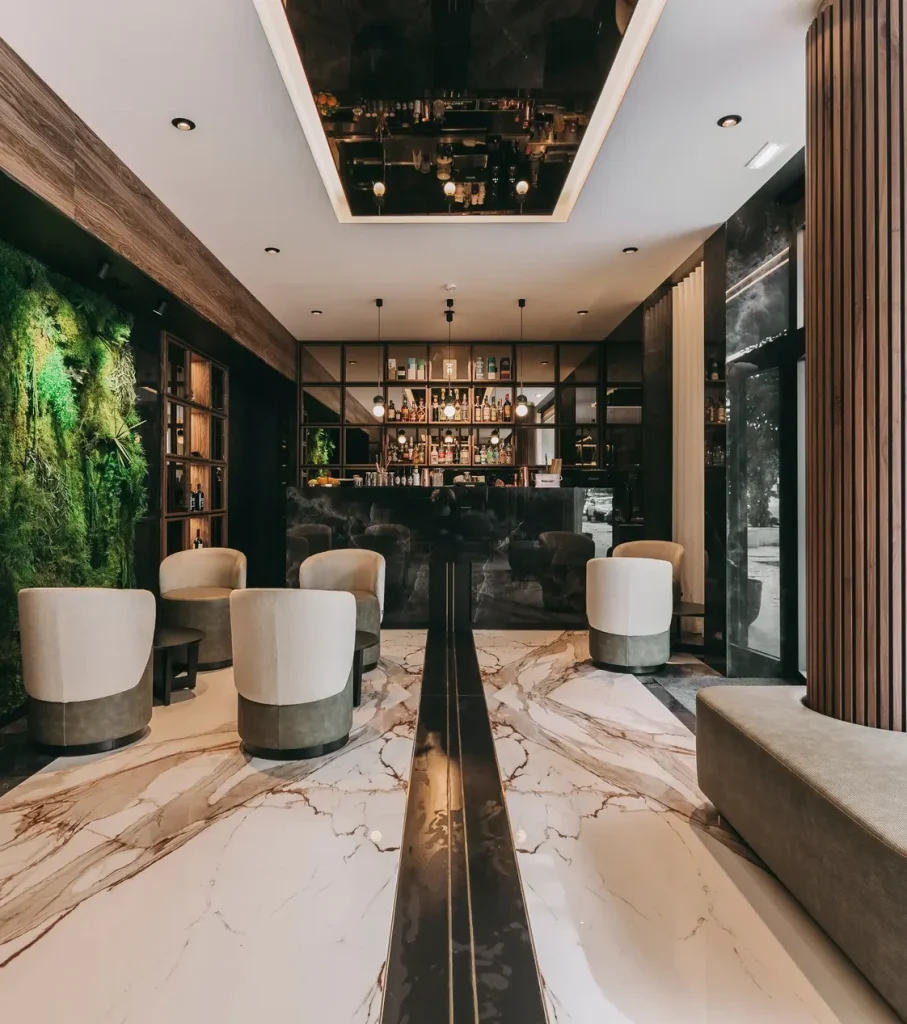 Modern bar lounge with plush chairs, marble floor, green wall, and a sleek bar counter.