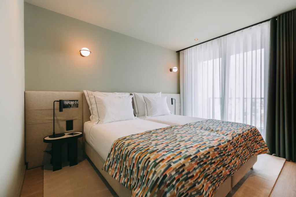 Modern hotel room with twin beds, colorful blanket, and soft lighting.
