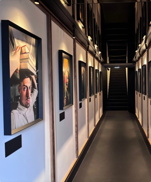 Art-lined hallway with portraits and a staircase at the end.