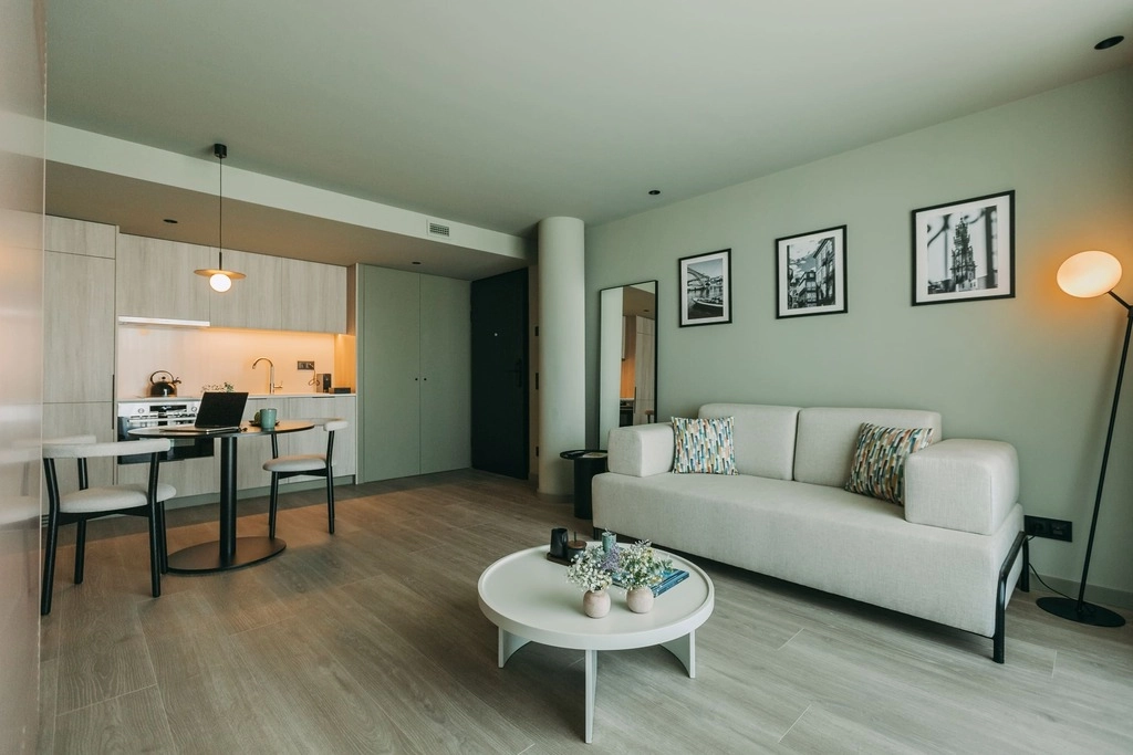 Modern living room with a sofa, round coffee table, and kitchen area in the background.