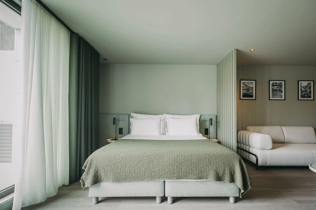 Modern bedroom with a double bed, green blanket, sofa, and framed pictures on the wall.