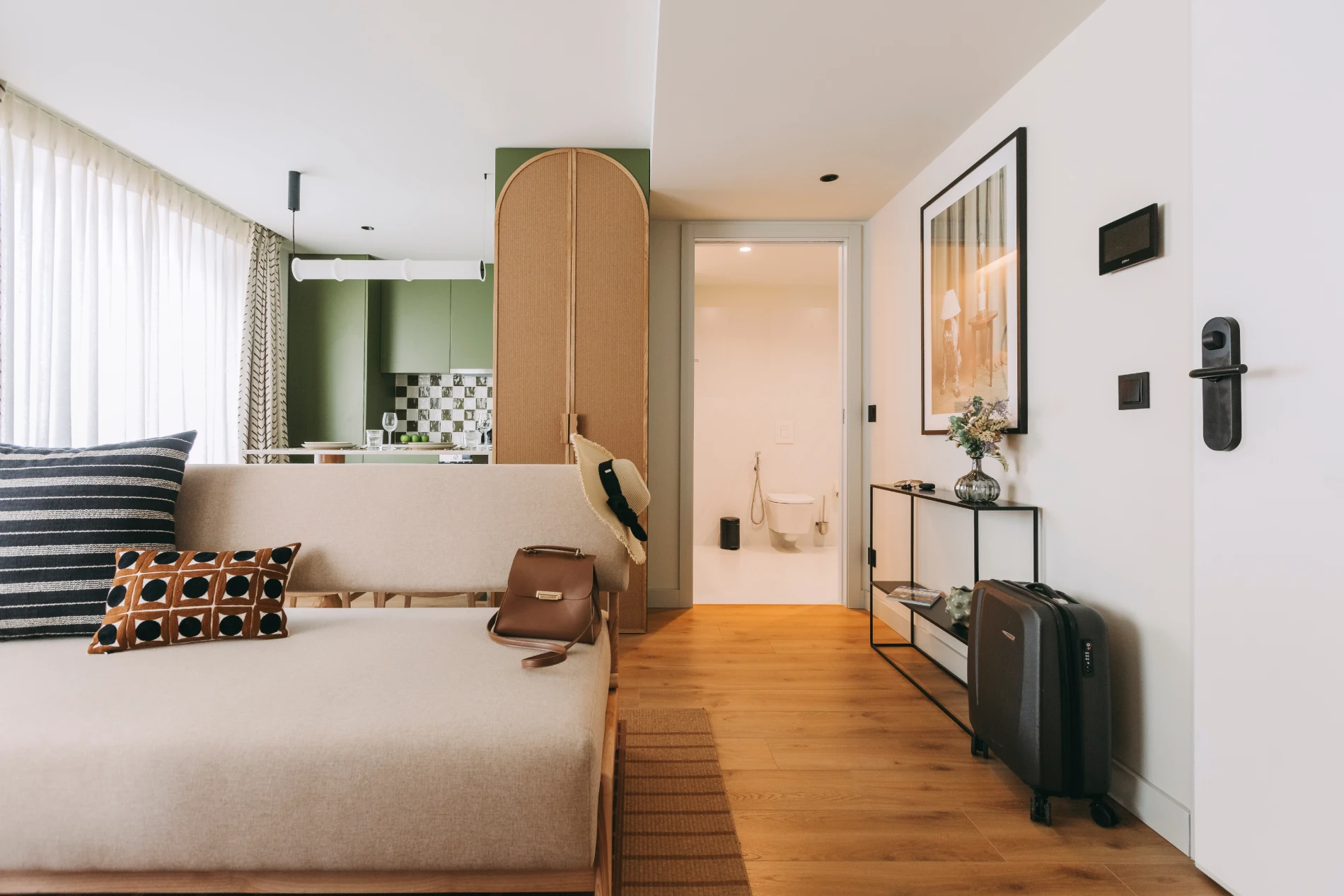 Modern apartment with a beige sofa, green kitchen, and suitcase in the hallway.
