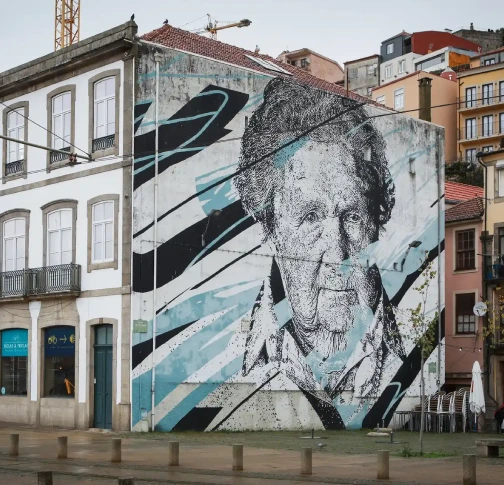 Large mural of an elderly man on a building's side in an urban area.