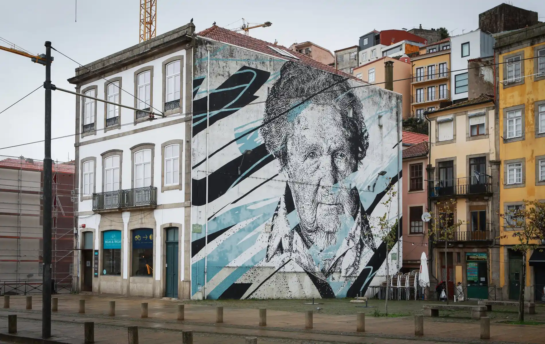 Mural of a woman's face on a building's side, with colorful abstract patterns in an urban setting.