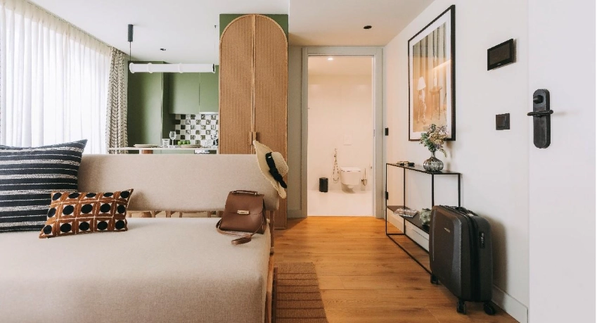 Modern apartment interior with sofa, kitchen, and hallway to a bathroom. Suitcase by the door.