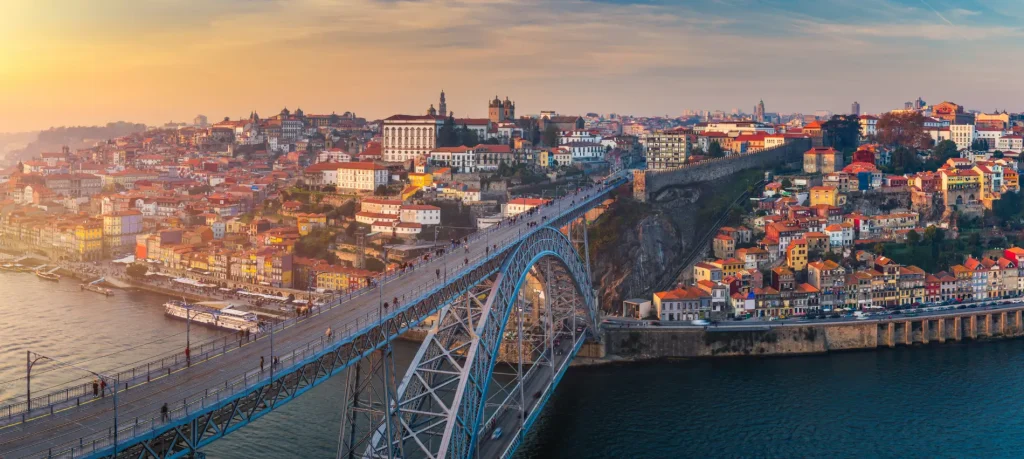 A sunset view of Porto, Portugal with a bridge over the Douro River and colorful buildings.