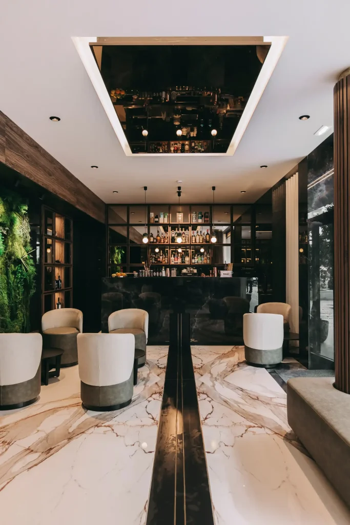 Elegant modern bar with marble floor, circular chairs, black counter, and green wall decor.