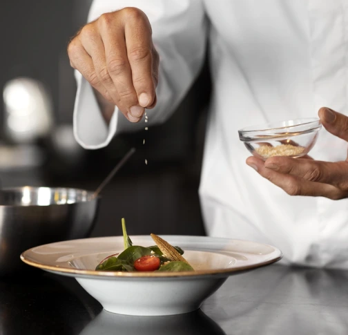 Chef seasoning a salad with greens and cherry tomatoes in a bowl.