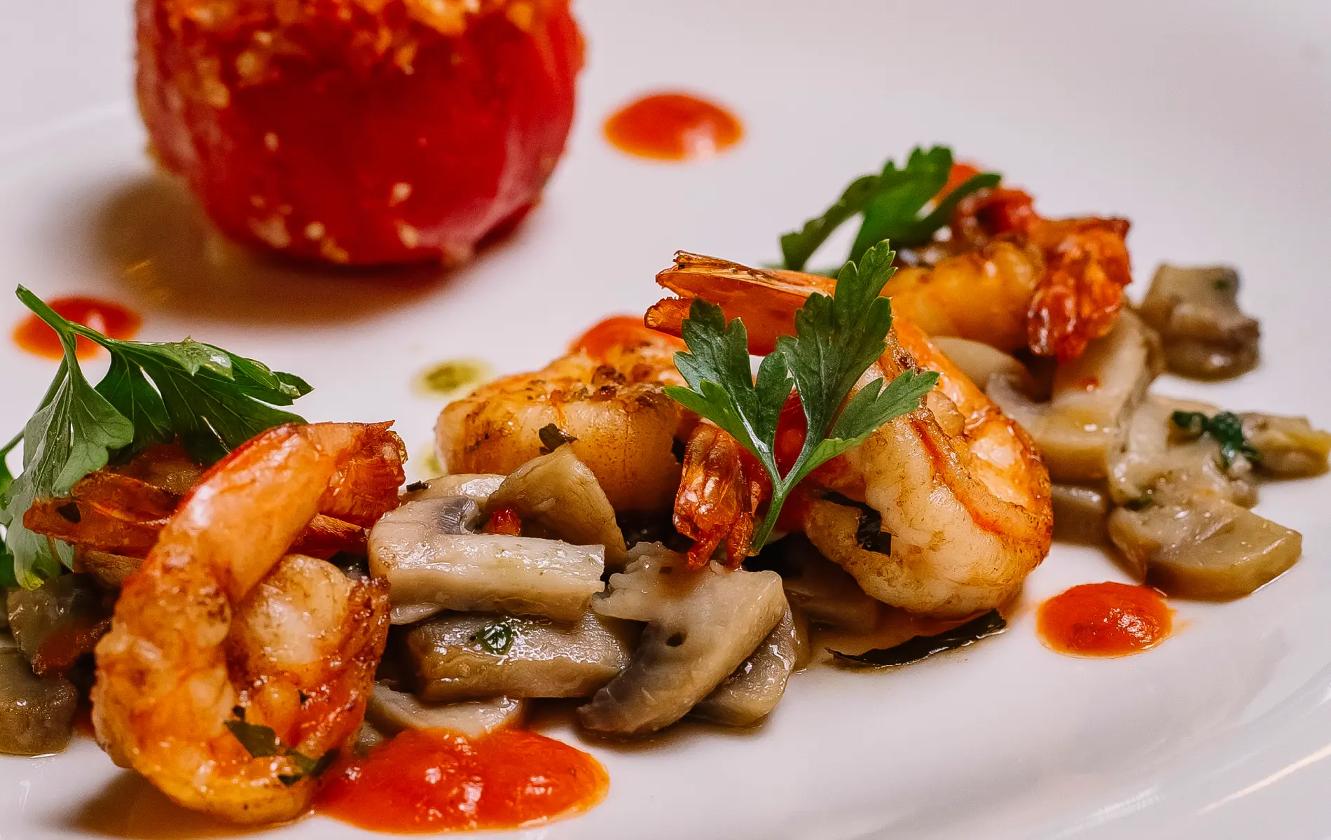 Grilled shrimp with mushrooms and tomato sauce on a white plate, garnished with parsley.