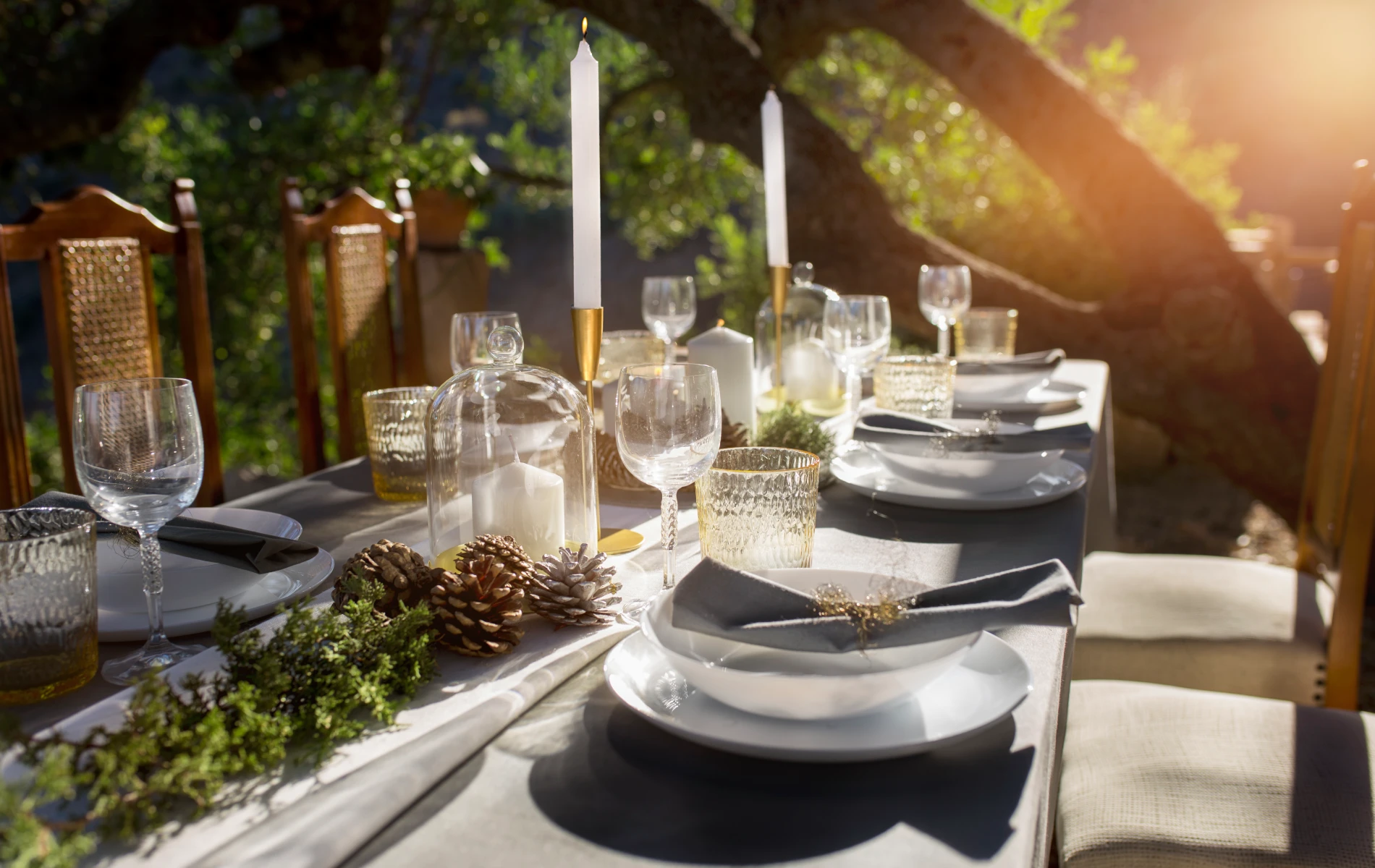 Elegant outdoor table setting with candles, pinecones, and glassware.