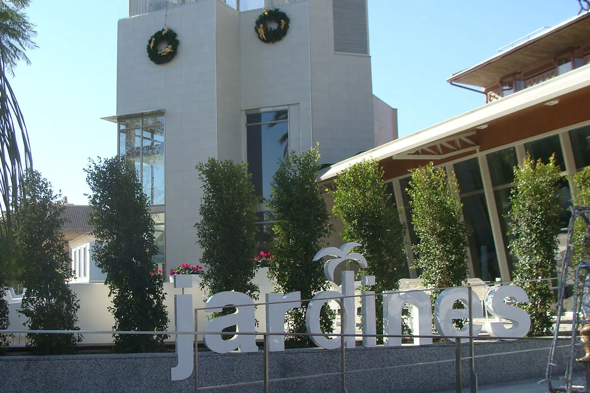 Edificio moderno con ventanas grandes y decoración navideña. Cartel que dice "jardines" en primer plano.