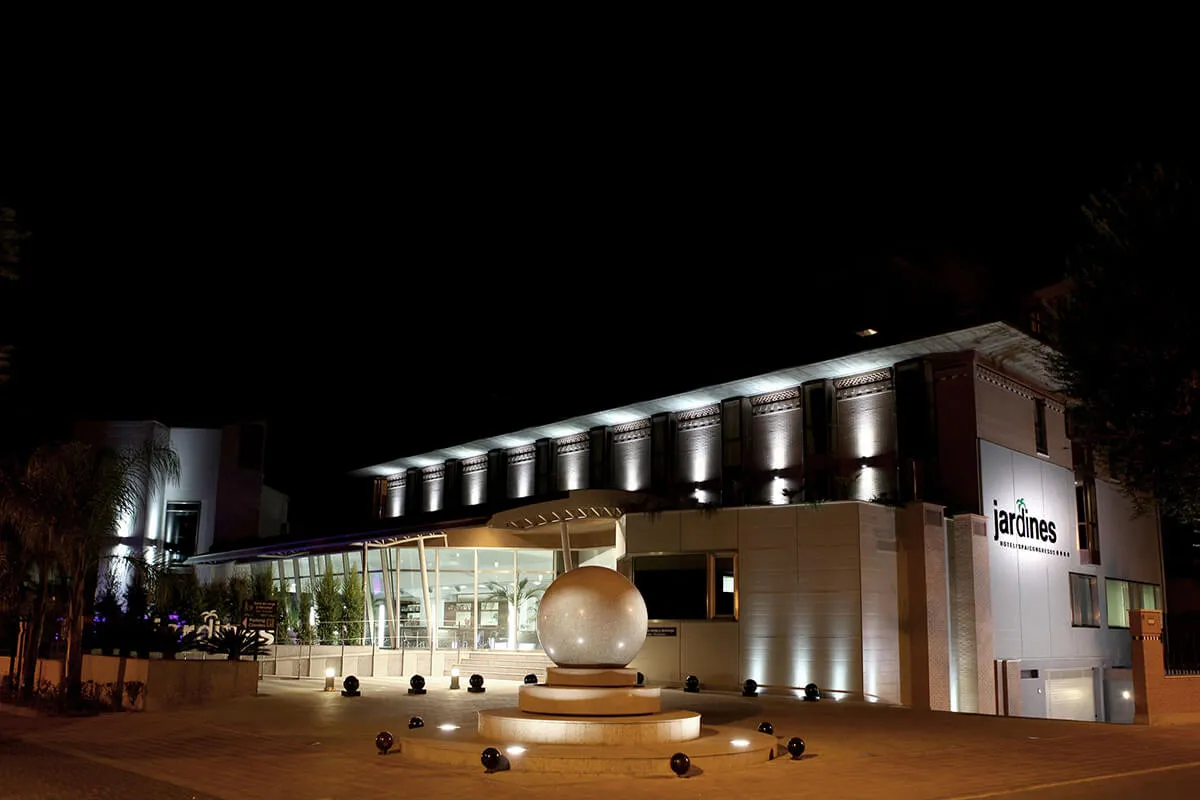 Edificio iluminado por la noche con fachada moderna y una escultura esférica frente a la entrada principal.