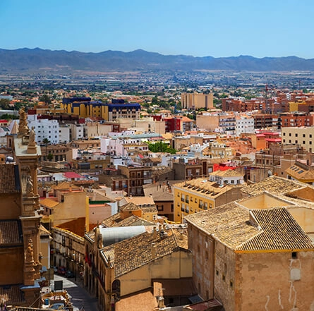 Vista panorámica de una ciudad con casas de techos de tejas y montañas al fondo bajo un cielo despejado.