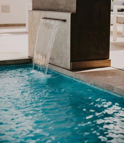 Cascada de agua cayendo en una piscina azul en un ambiente interior elegante y bien iluminado.