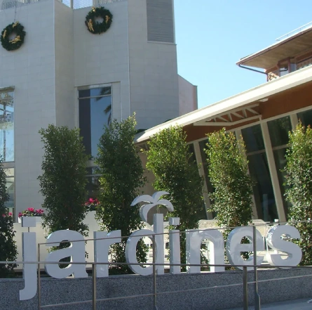 Fachada de un edificio moderno con letrero de "jardines" y decoraciones navideñas en la parte superior.