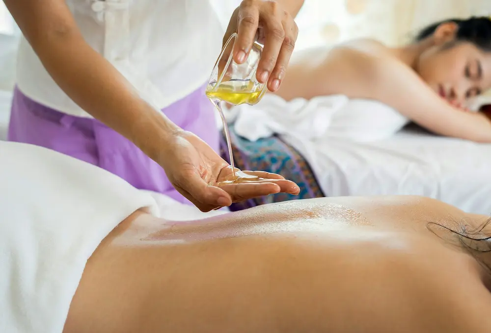 Persona recibiendo un masaje con aceite mientras otra descansa al fondo, en un ambiente relajante de spa.