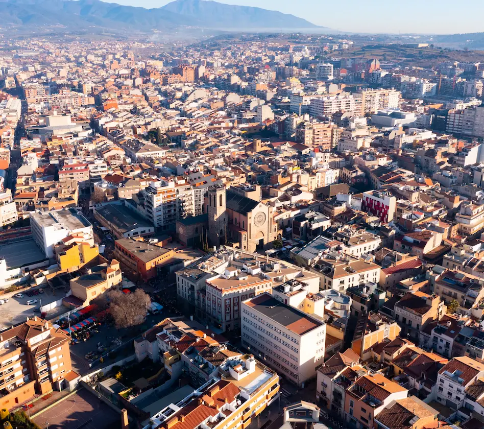Vista aérea de una ciudad con una iglesia destacada en el centro, rodeada de edificios y montañas al fondo.